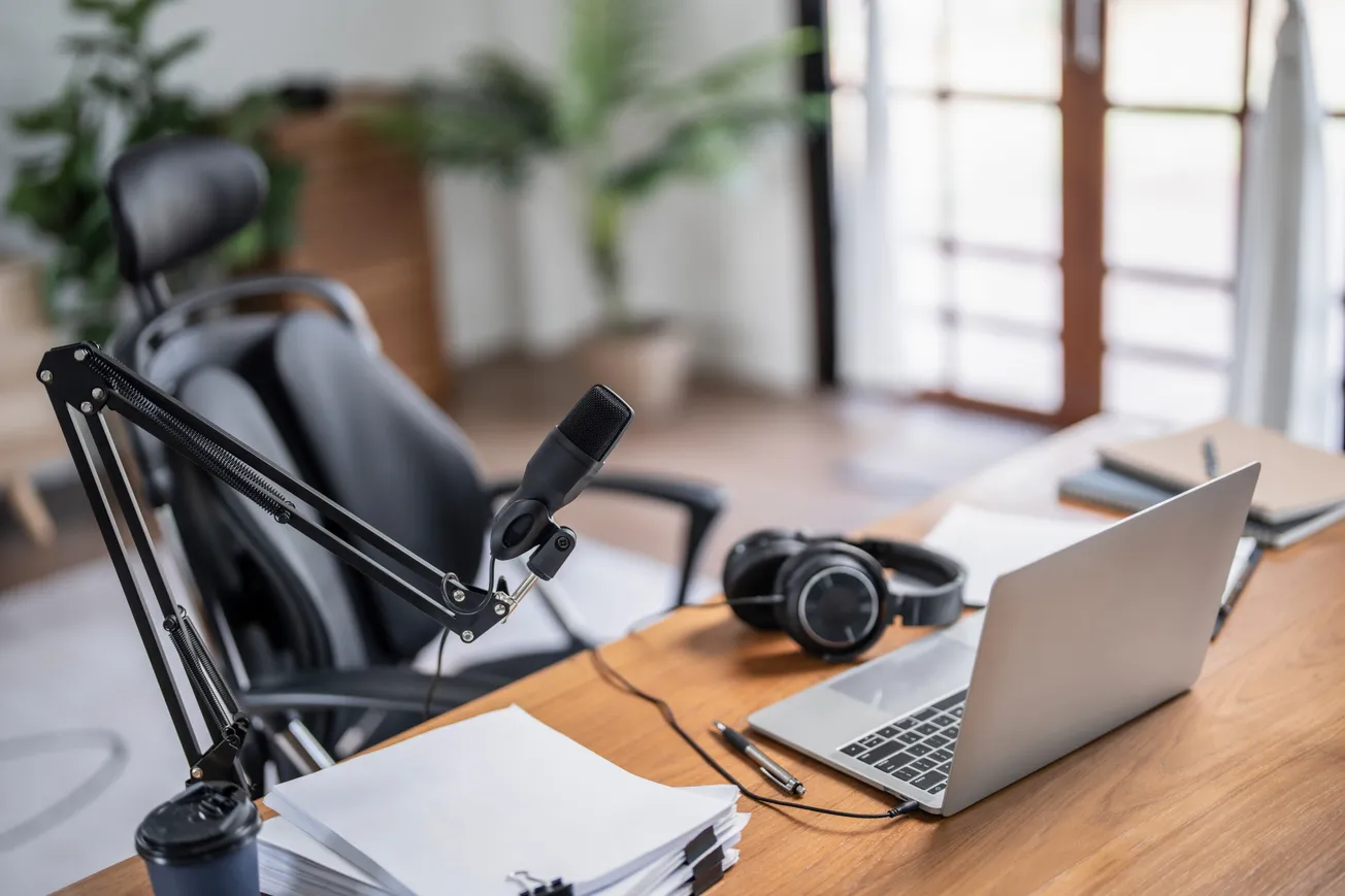Home podcast recording setup with microphone, headphones, and laptop on wooden desk.Digital media production workspace.