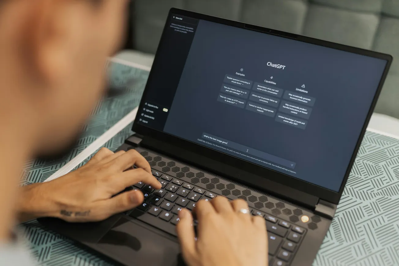 A person types on a laptop displaying the ChatGPT interface with a patterned blue table in the background.