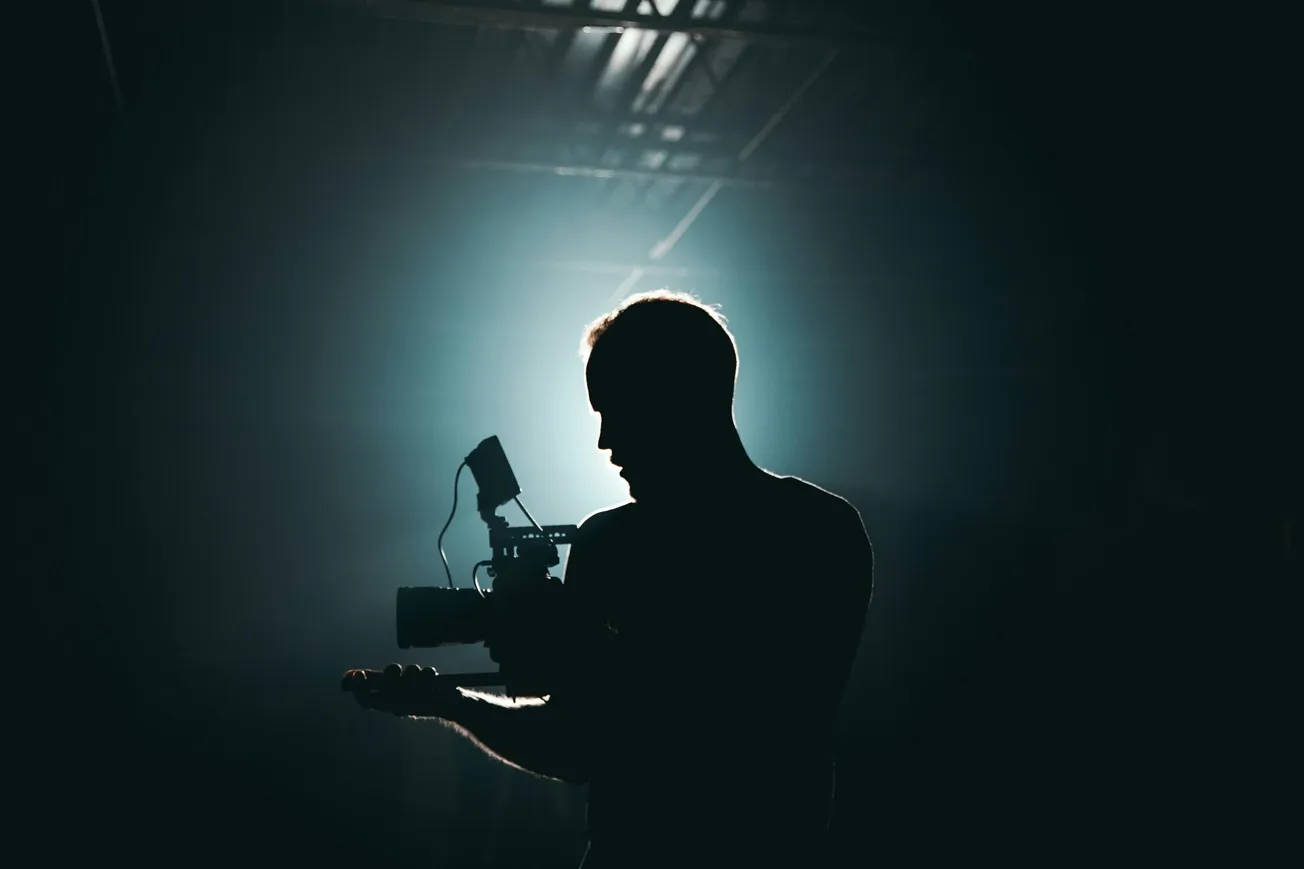 Silhouette of a person holding a camera against a dimly lit background with soft lighting.