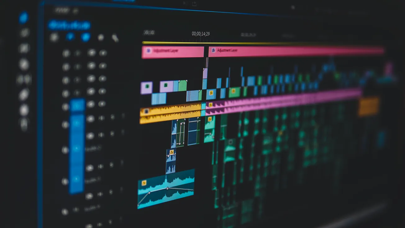 Close-up of a video editing software timeline on a computer screen, featuring colorful layers and waveforms.