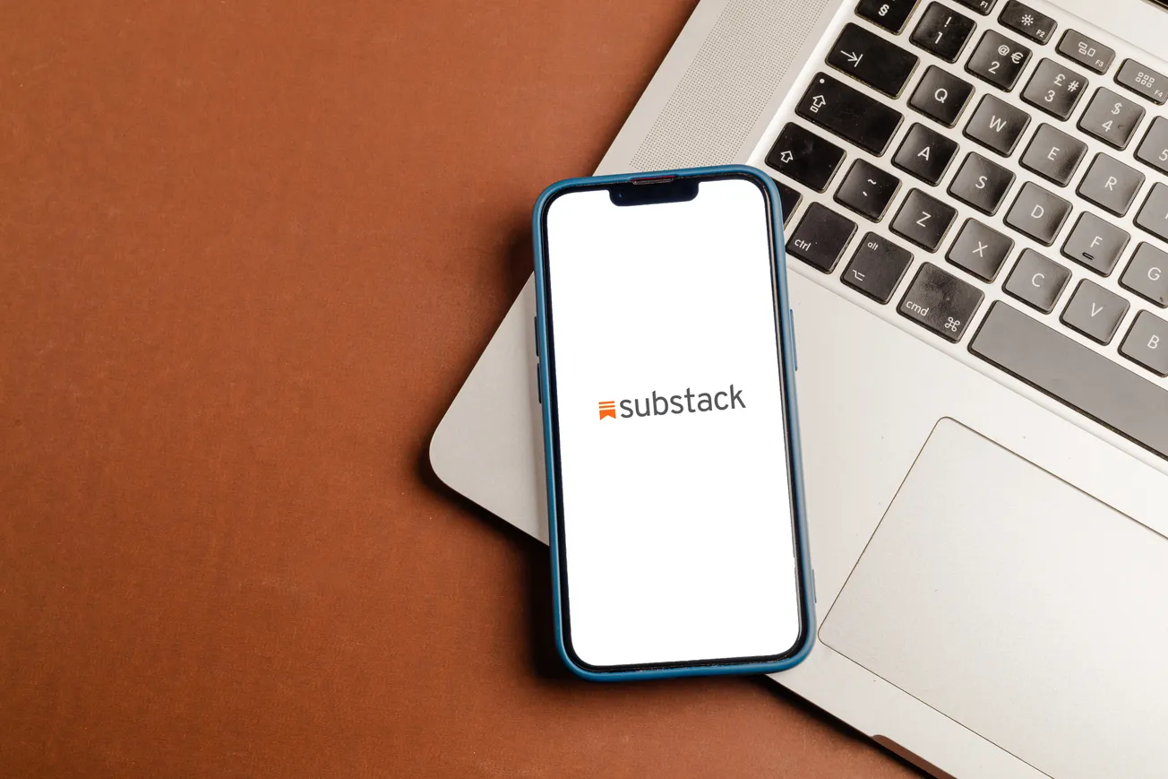 An iPhone displaying the Substack logo rests on an open laptop keyboard.