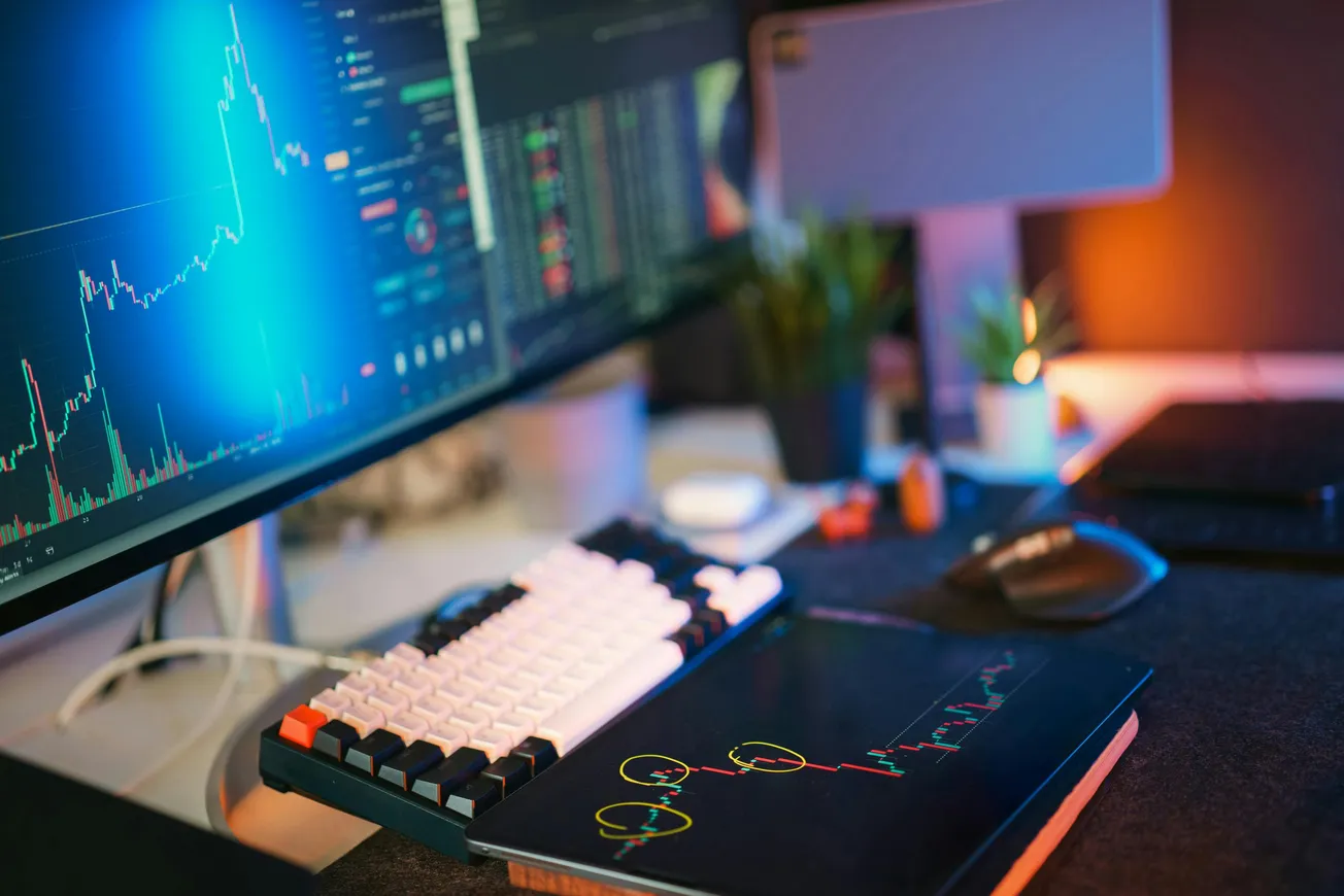 Modern workspace with a computer monitor showing stock charts, tablet with graphs, mechanical keyboard, mouse, and soft lighting.