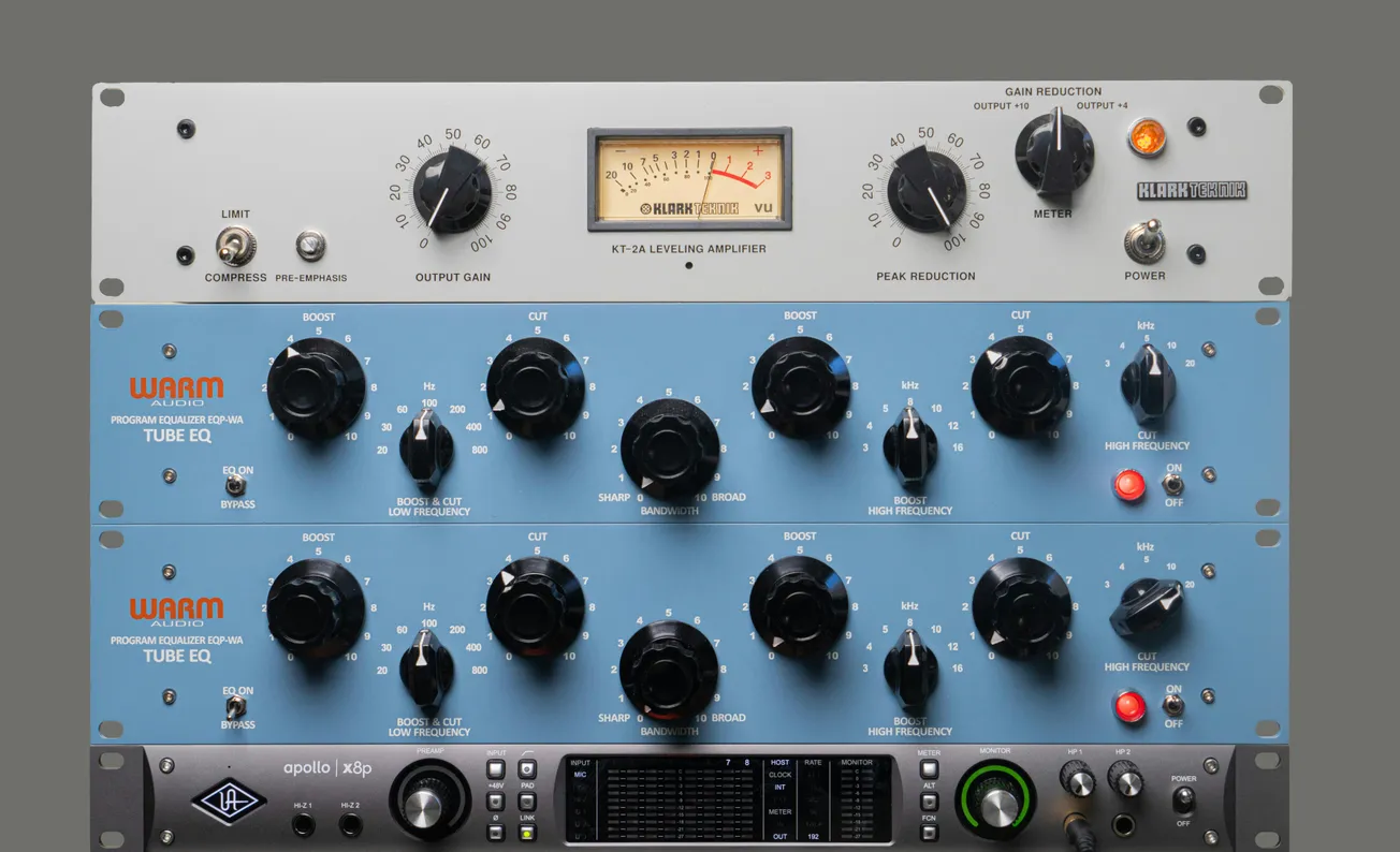 Stacked audio equipment featuring a silver KT-2A leveling amplifier with a VU meter, two blue Warm Audio EQ units, and a black Apollo x8p interface.