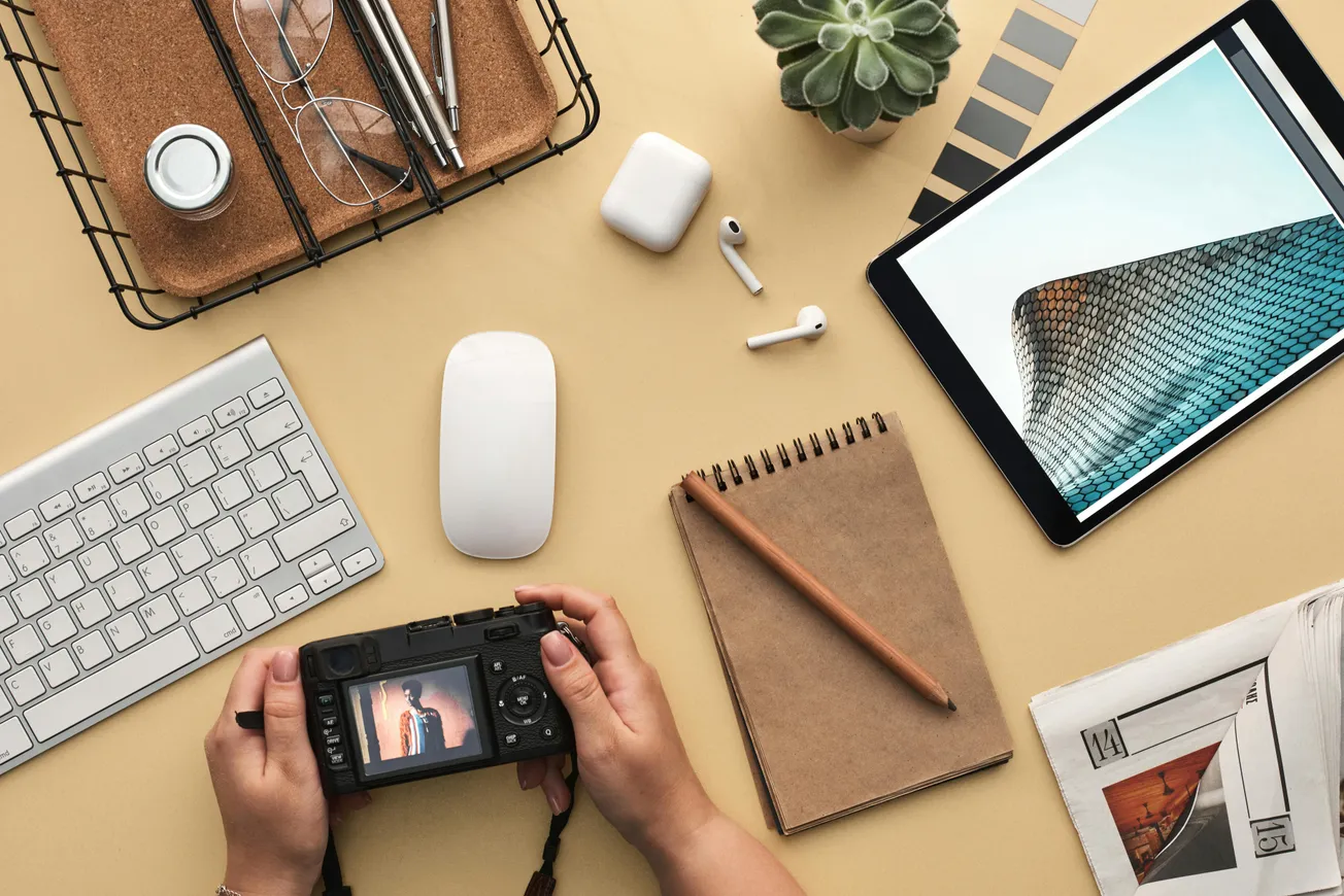 A workspace with a keyboard, camera, notepad, and tablet displaying a building. Items are neatly arranged, evoking creativity and organization.