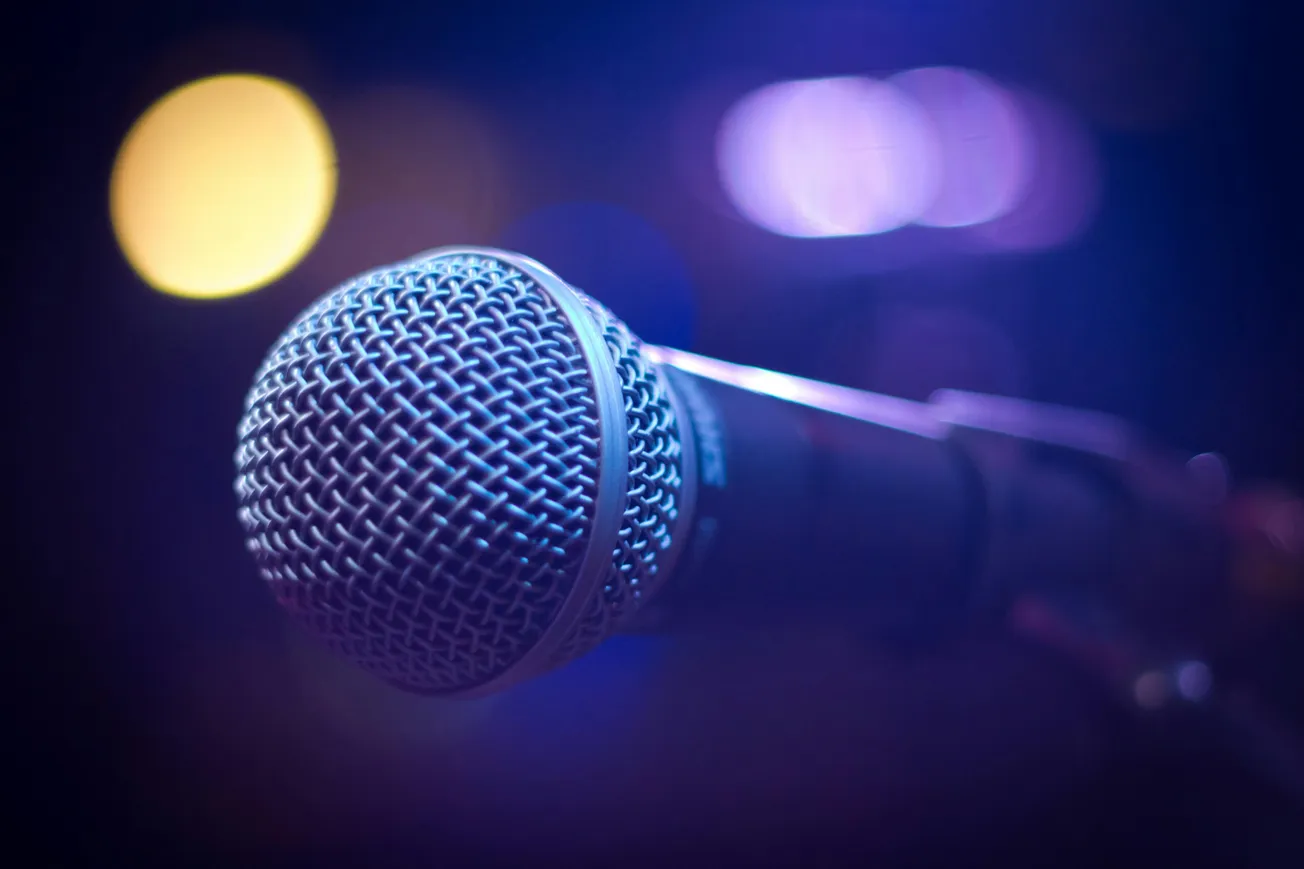 Close-up of a microphone in soft blue and purple lighting, with a blurred yellow light in the background, conveying a moody, musical atmosphere.