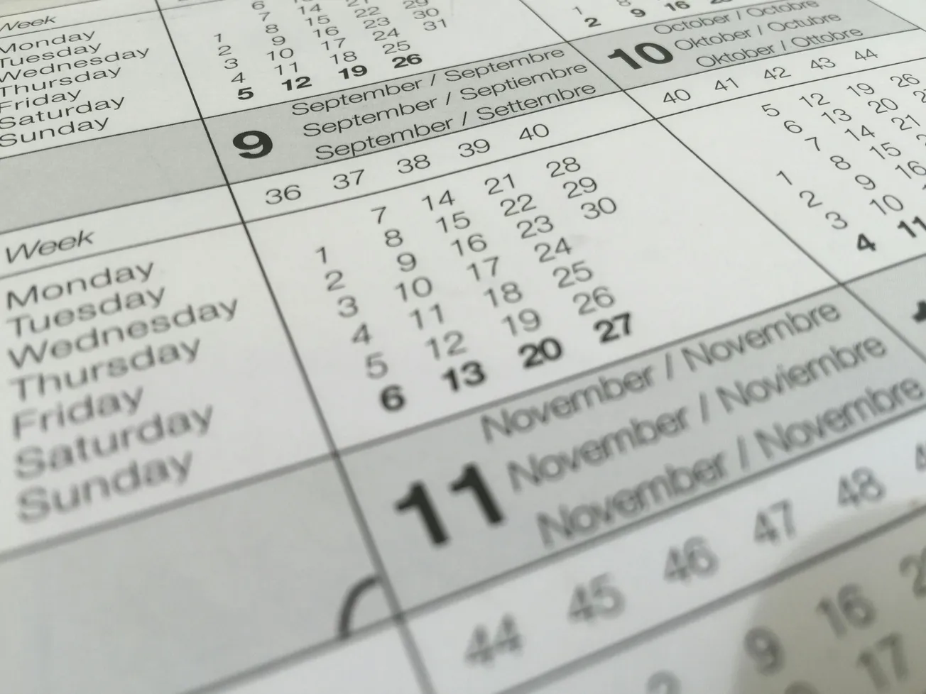 Close-up of a calendar showing months in multiple languages, focusing on September to November dates. The layout suggests an organized, planning theme.