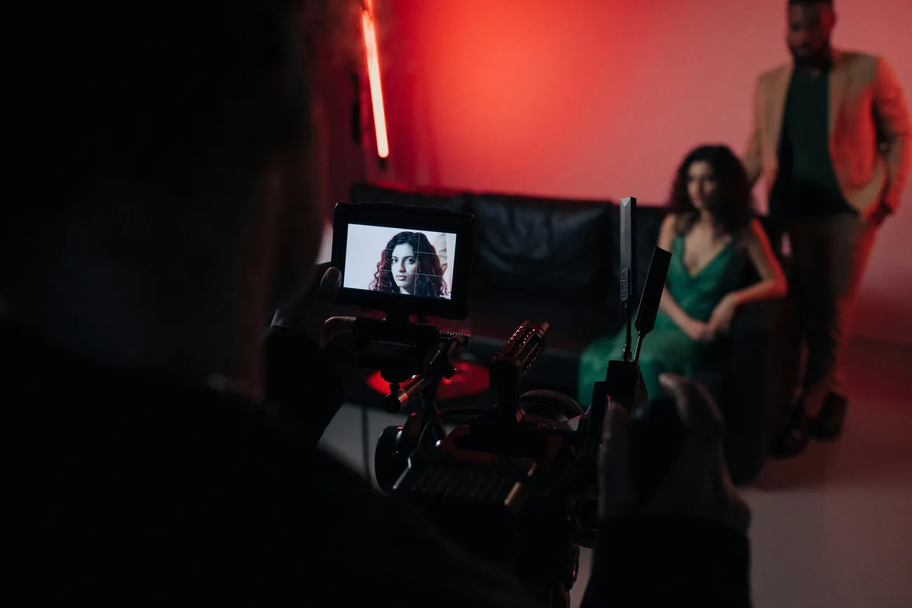 A camera display shows a woman in focus, with long hair, seated on a black couch. She is wearing a green dress. The scene is bathed in red light.