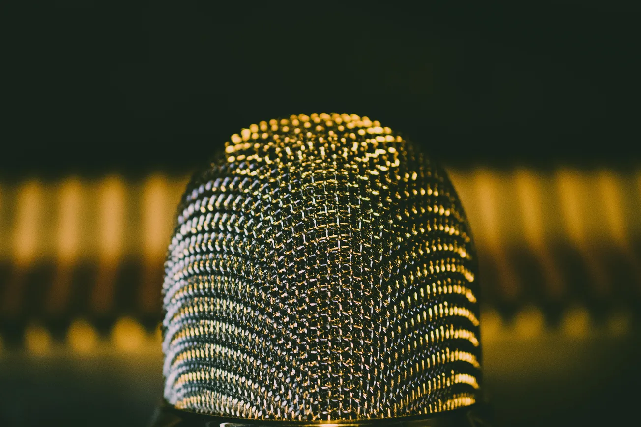 Close-up of a vintage microphone with a textured metal grille, warmly lit against a blurred, gold-toned background, creating a nostalgic ambiance.