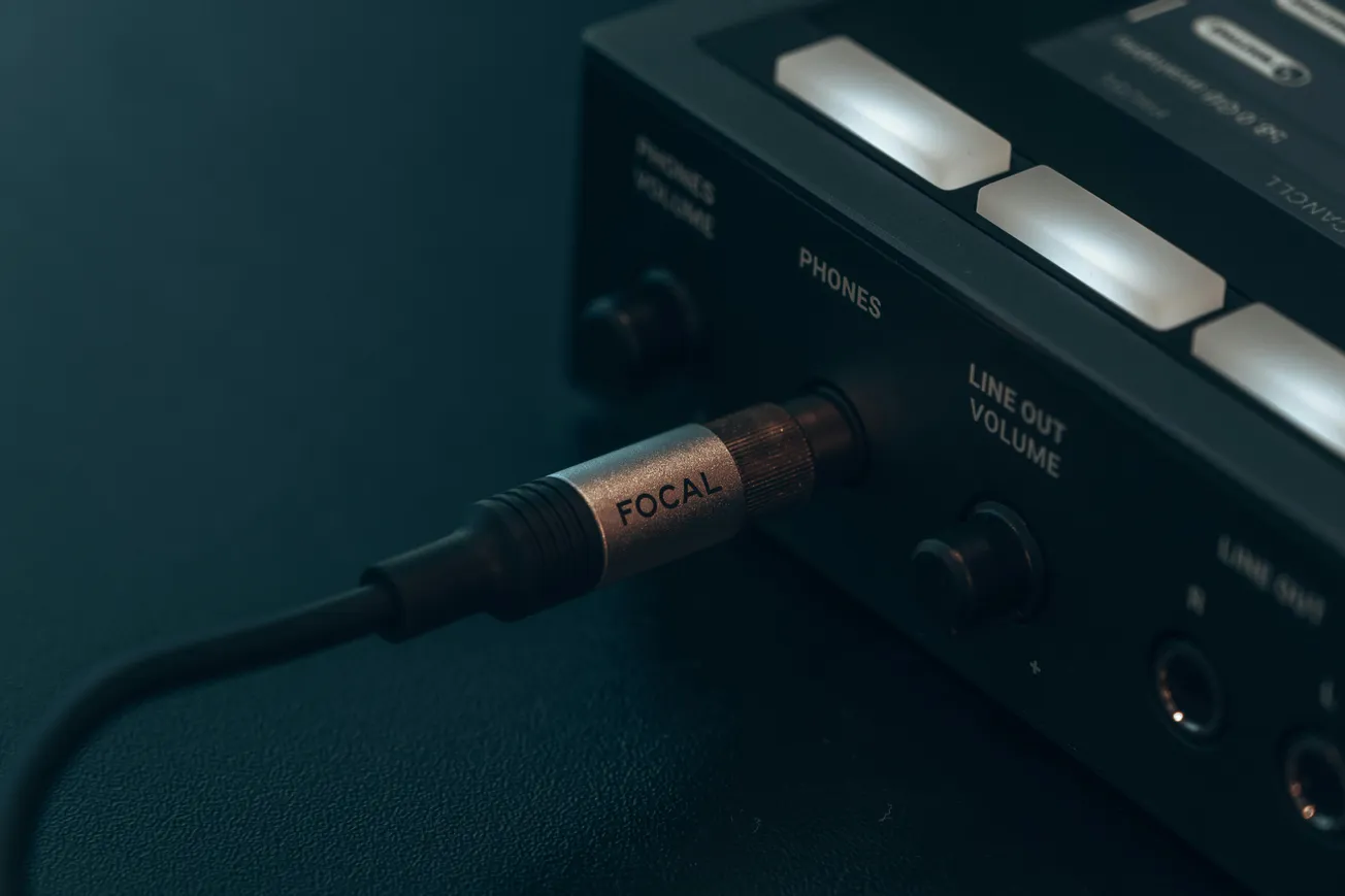 Close-up of a headphone cable labeled "FOCAL" plugged into the "PHONES" jack of a sleek black audio device. Soft lighting creates a focused, professional tone.