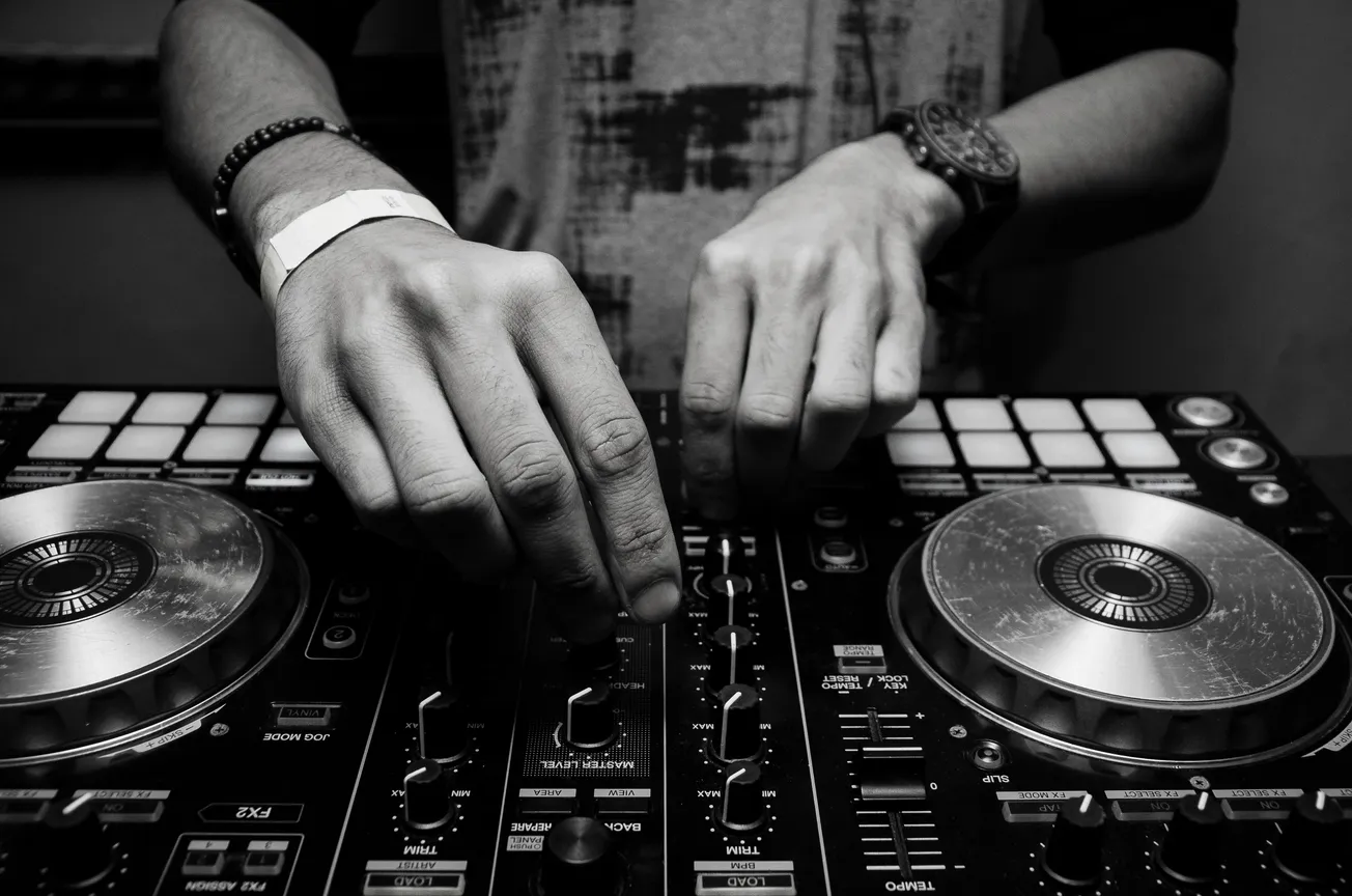 Close-up of hands adjusting controls on a DJ mixer, conveying focus and creativity. The black and white tone adds a classic, artistic feel.