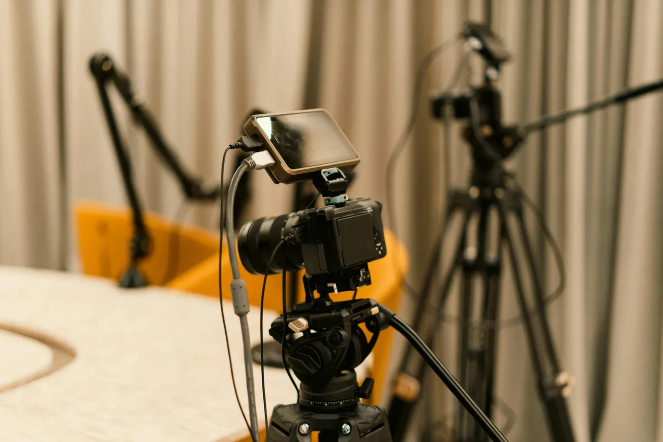 A professional video camera setup in a studio, surrounded by microphones and a tripod against a backdrop of gray curtains, conveys a focused, production-ready atmosphere.