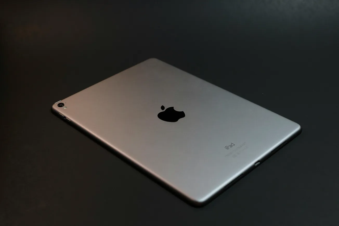 The image depicts a sleek, silver iPad resting on a dark surface. It features the Apple logo prominently, suggesting a minimalist and modern aesthetic.