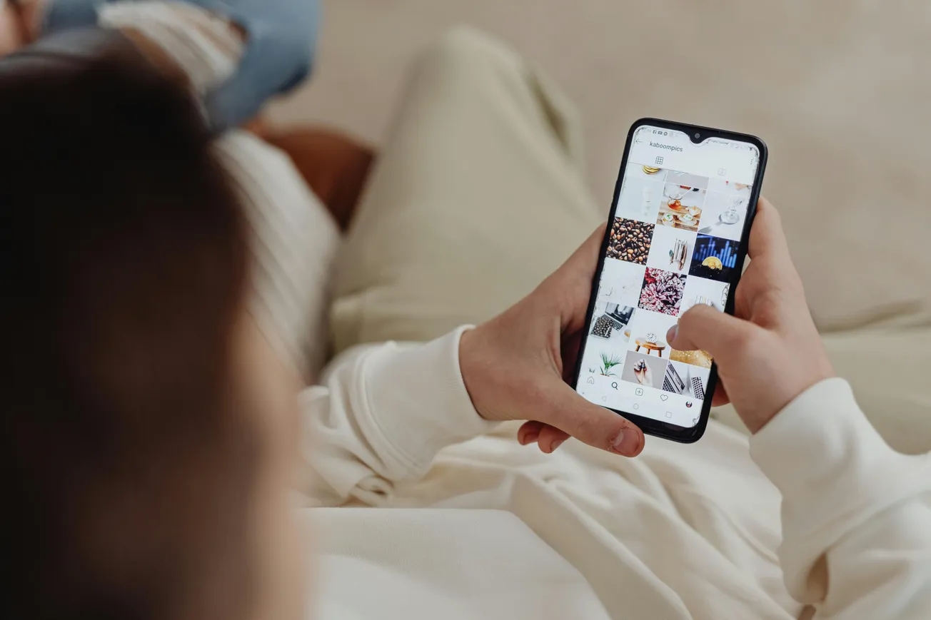 A person in a white sweater holding a smartphone, browsing an image gallery with various colorful thumbnails. The tone is relaxed and casual.
