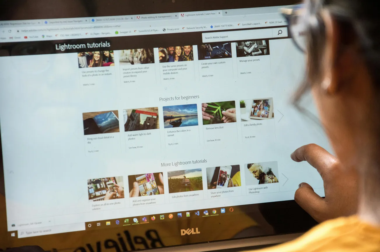 A person using a Dell laptop browses Adobe Lightroom tutorials online. The screen displays tutorial categories and images, suggesting an educational focus.