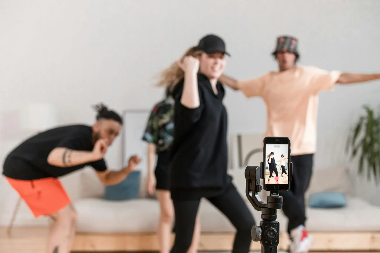 Three people dance energetically in a living room, captured by a smartphone on a tripod. The atmosphere is lively and playful.