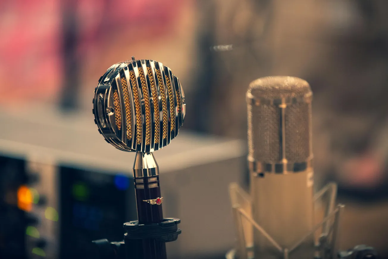 Retro style microphone with chrome grille beside a modern condenser microphone in a recording studio, evoking a vintage yet professional ambiance.