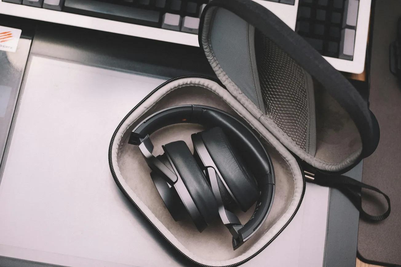 Black headphones rest in an open gray case on a desk, next to a computer keyboard. The scene suggests readiness for work or play.