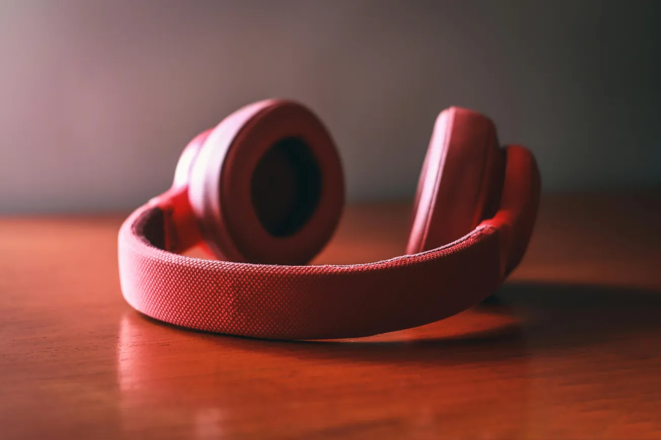 A pair of red over-ear headphones rests on a wooden table. The scene is warmly lit, highlighting the textured fabric and creating a cozy, inviting atmosphere.