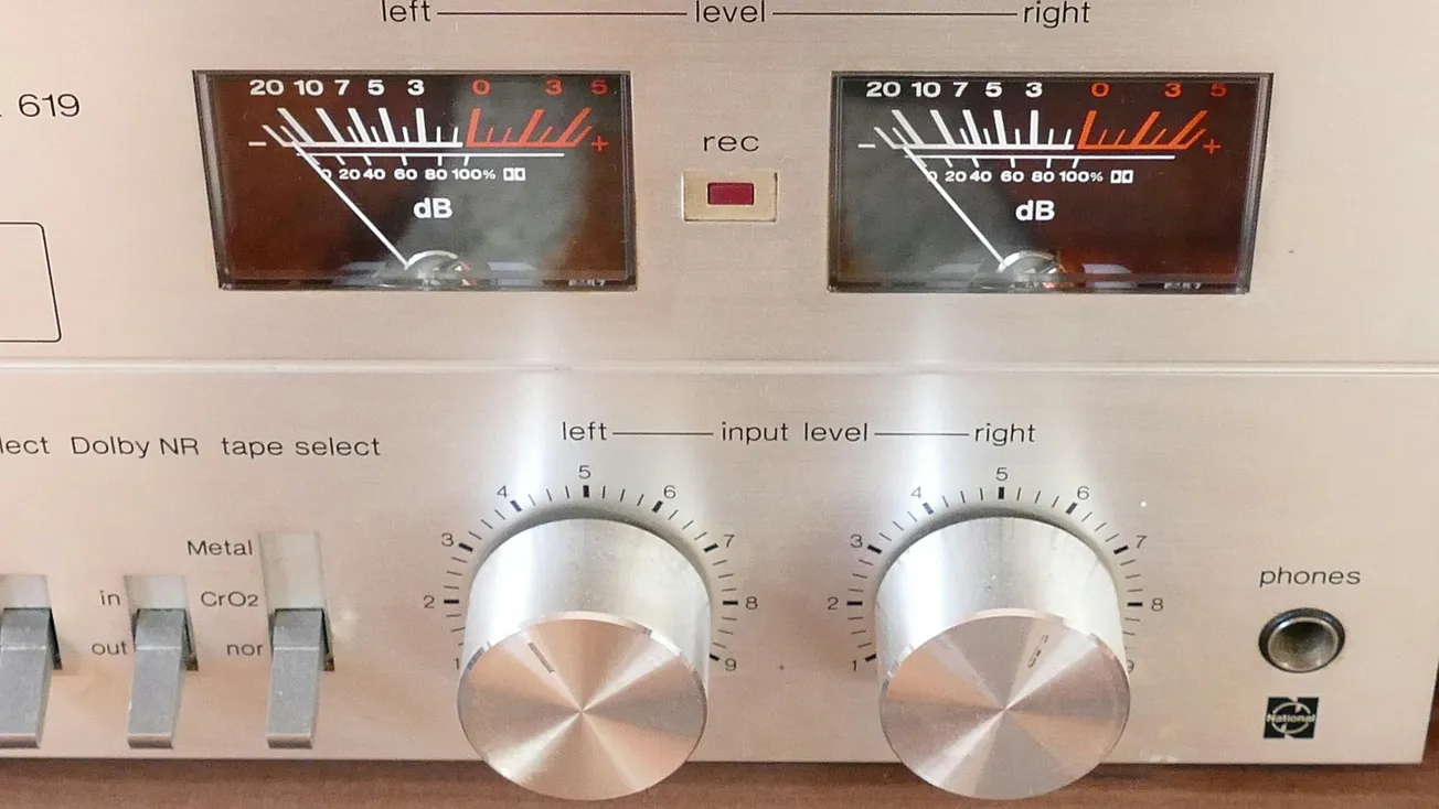 Close-up of a vintage audio receiver showing two analog VU meters, control dials, and switches. Labels include "input level" and "Dolby NR." Buttons have a metallic finish.
