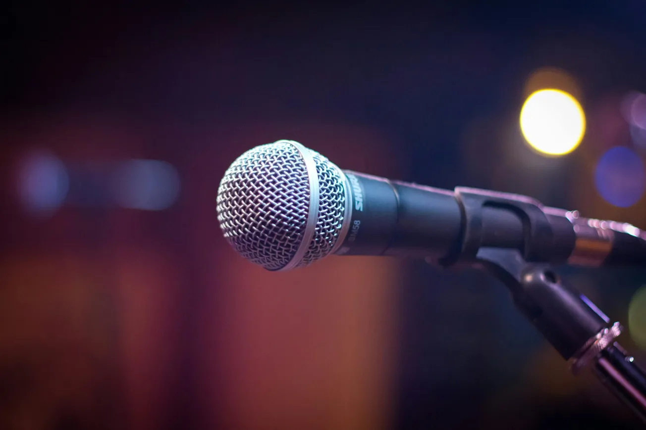 Close-up of a microphone on a stand against a blurred background with colorful bokeh lights, evoking a lively, performance-ready atmosphere.
