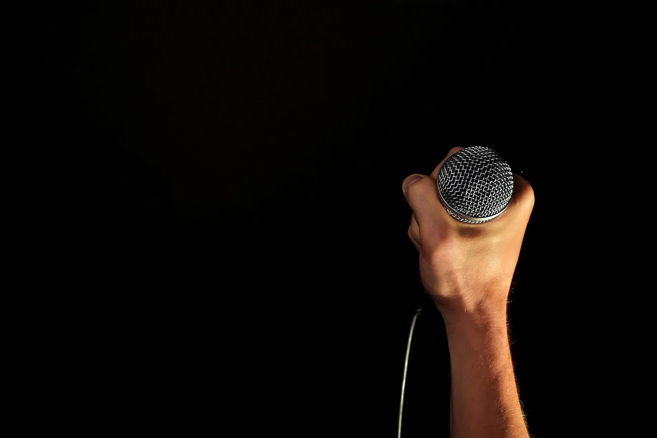 A hand gripping a microphone stands out against a dark background, evoking a sense of anticipation and performance.