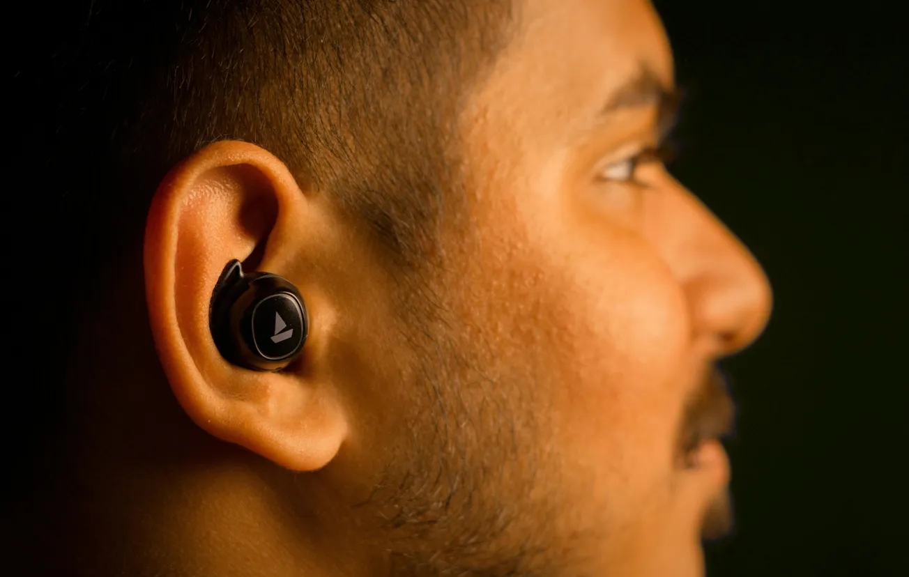 Profile of a person wearing a black wireless earbud, set against a dark background. The scene conveys a sense of focus and modern technology use.