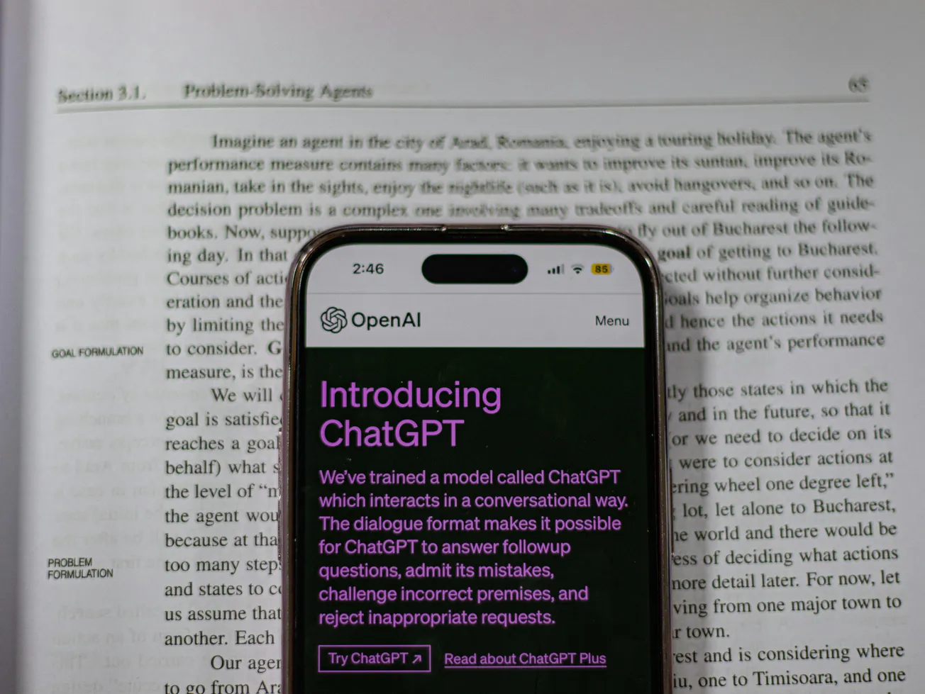 A smartphone displays the OpenAI ChatGPT introduction screen over an open book about "Problem-Solving Agents," combining tech and academic themes.