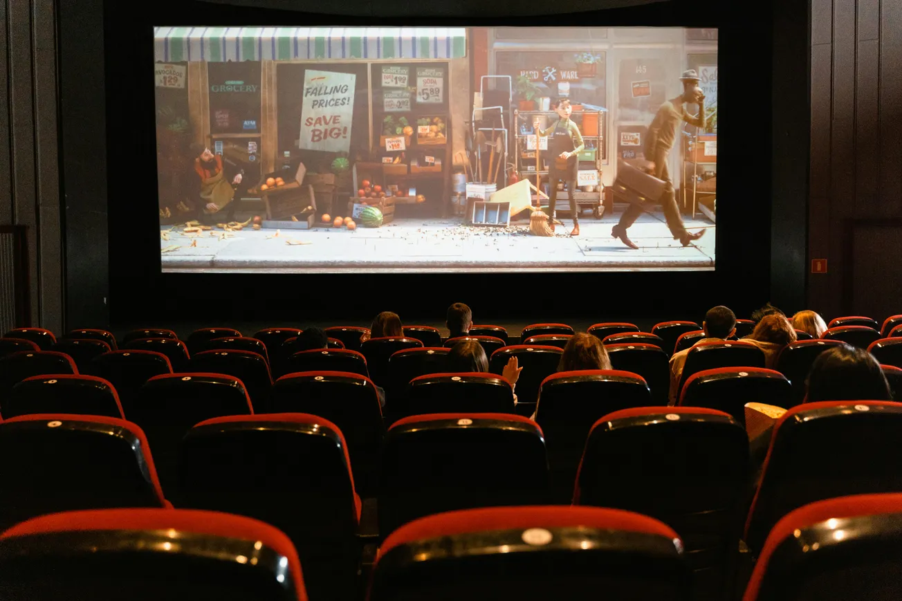 A nearly empty movie theater shows a film with a storefront scene. Few audience members are seated; the ambiance is quiet and focused.