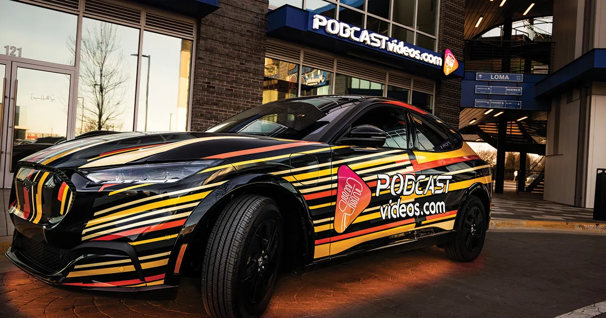 A colorful car with vibrant orange and yellow stripes is parked outside a building. The car features the logo "PODCASTvideos.com" prominently displayed.