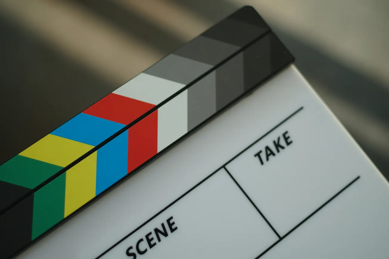 Close-up of a colorful film clapperboard with diagonal stripes. It shows the sections for "Scene" and "Take," evoking a filmmaking atmosphere.