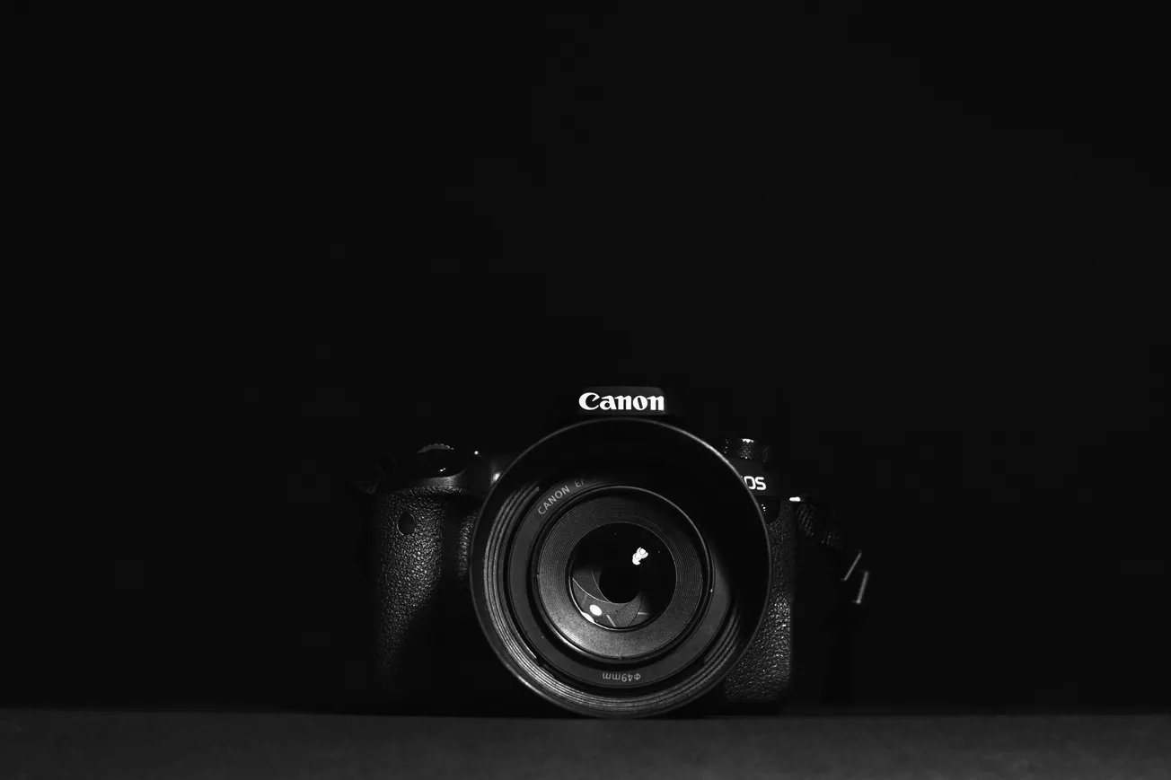 A Canon camera is centered against a black background, with its lens prominently visible. The image has a sleek, professional tone with dramatic lighting.