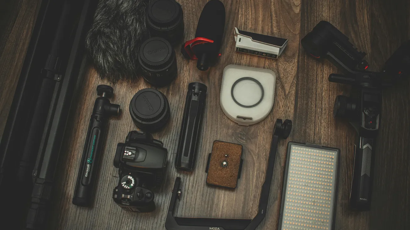 Alt text: A collection of photography equipment, including cameras, lenses, tripod, microphone, and LED light, arranged neatly on a wooden surface.