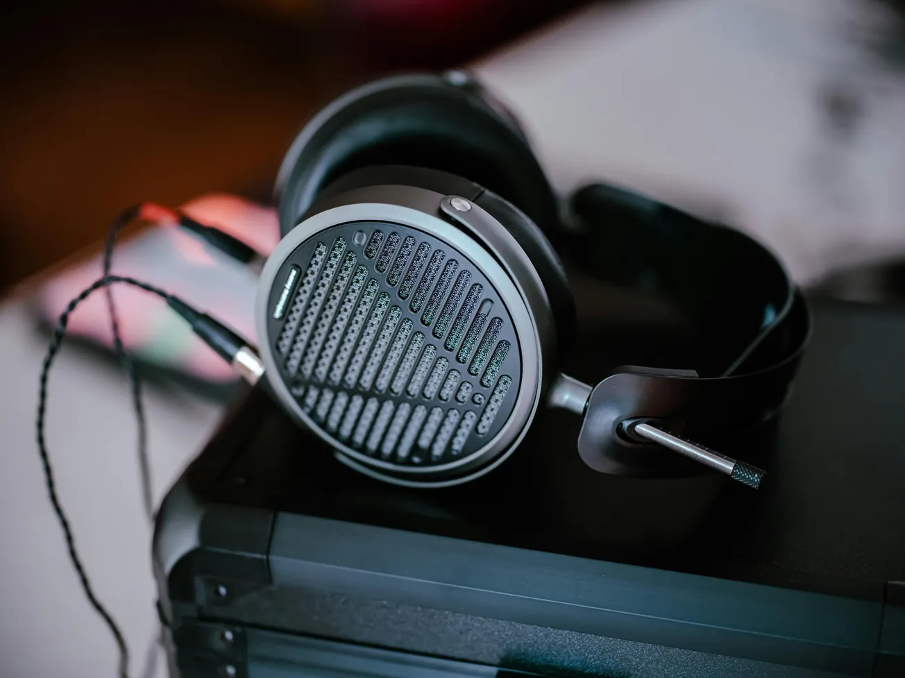 Sleek black headphones rest on a dark surface, with a mesh design and attached cable. The setting appears calm and modern, emphasizing high-quality audio.