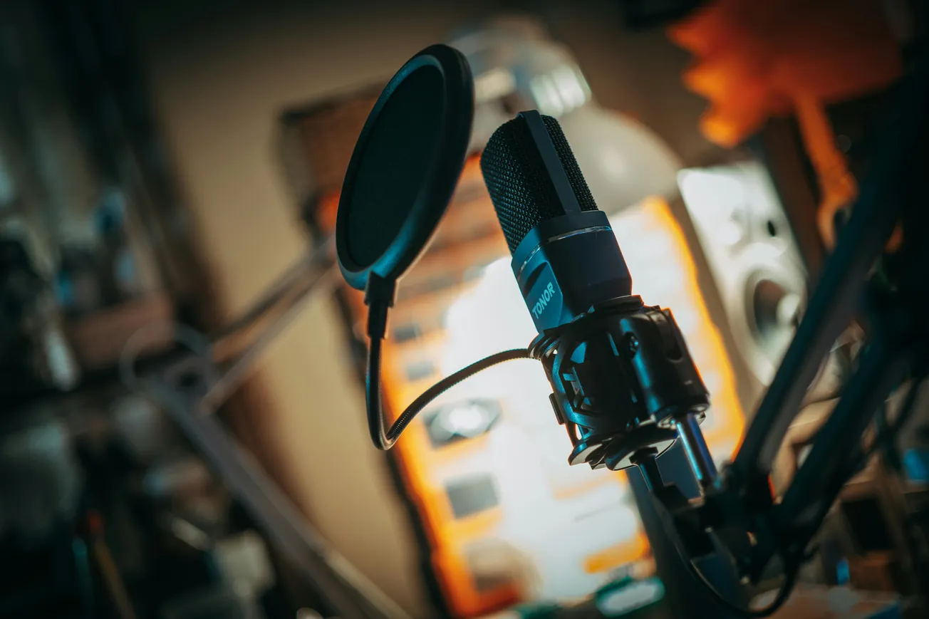 Close-up of a professional microphone with a pop filter in a studio. The background is softly blurred, creating a focused and creative atmosphere.