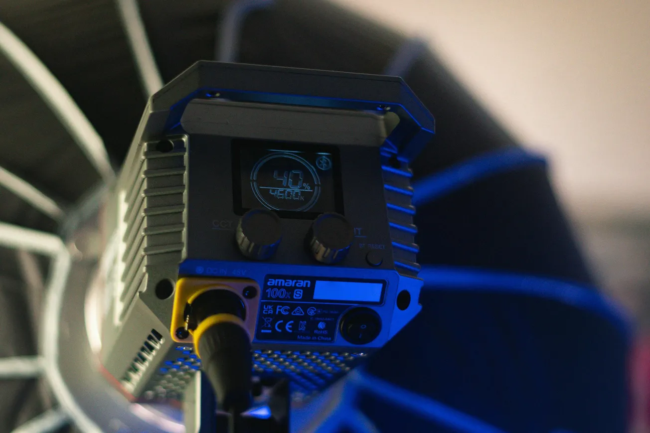 Close-up of a studio light with a digital display showing "40%". The background is softly blurred, with a cool blue tone, conveying a techy ambiance.