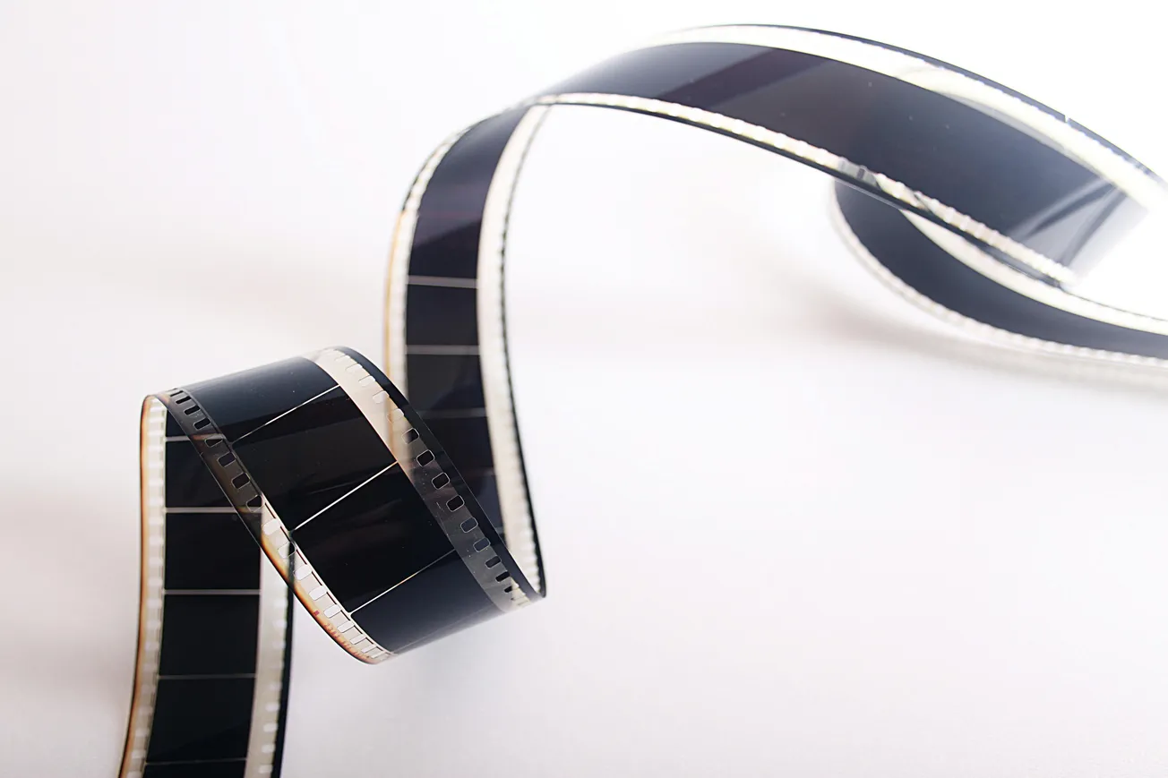 Curved strip of black film with perforated edges on a white background. The film bends gracefully, evoking a sense of nostalgia and creativity.