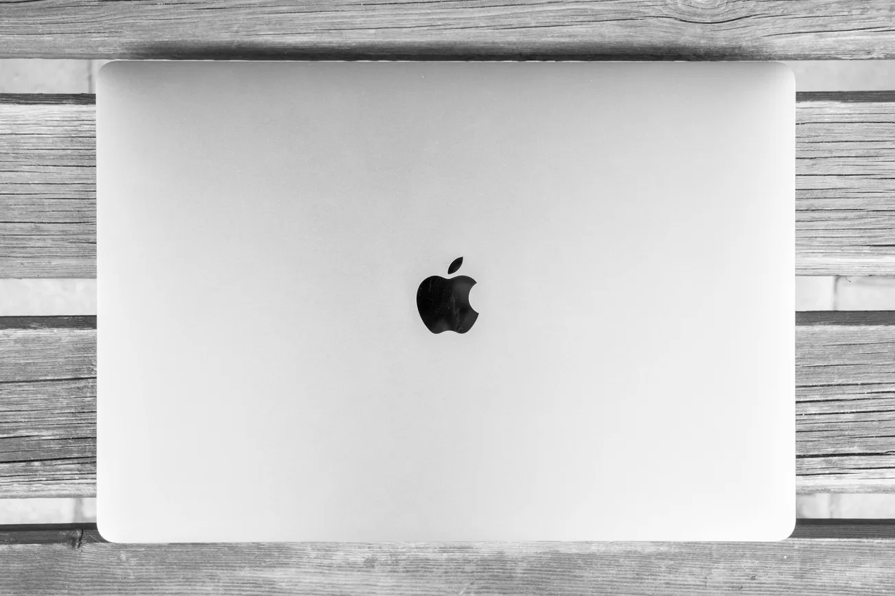 A closed silver laptop with an apple logo on a wooden surface. The minimalist design conveys a sleek, professional, and modern aesthetic.