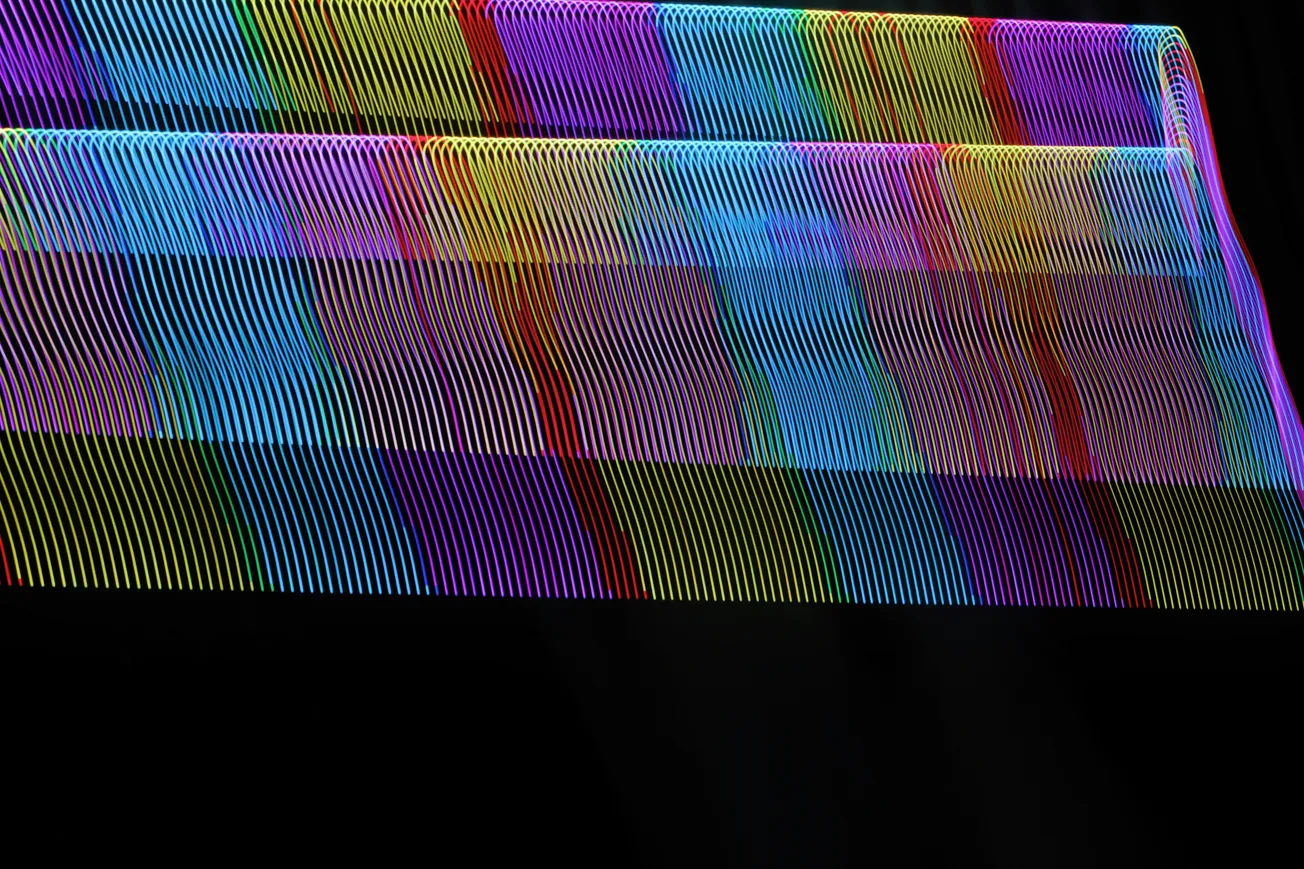 Abstract image of wavy, overlapping neon lines in a spectrum of colors on a black background. The pattern creates a vibrant, dynamic visual effect.