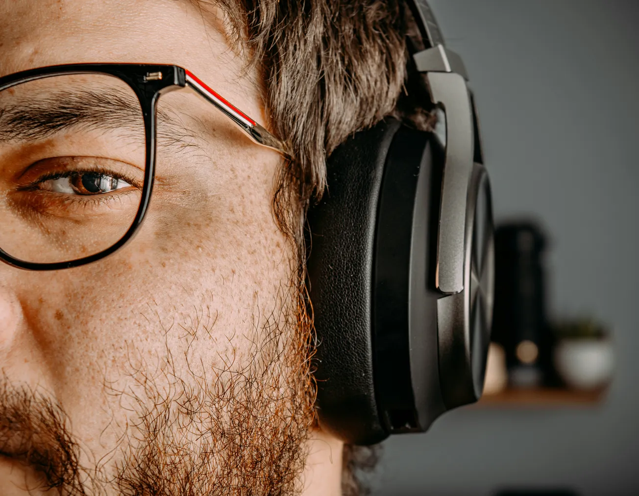 Close-up of a person wearing glasses and large headphones, focusing on their eye and headphones.