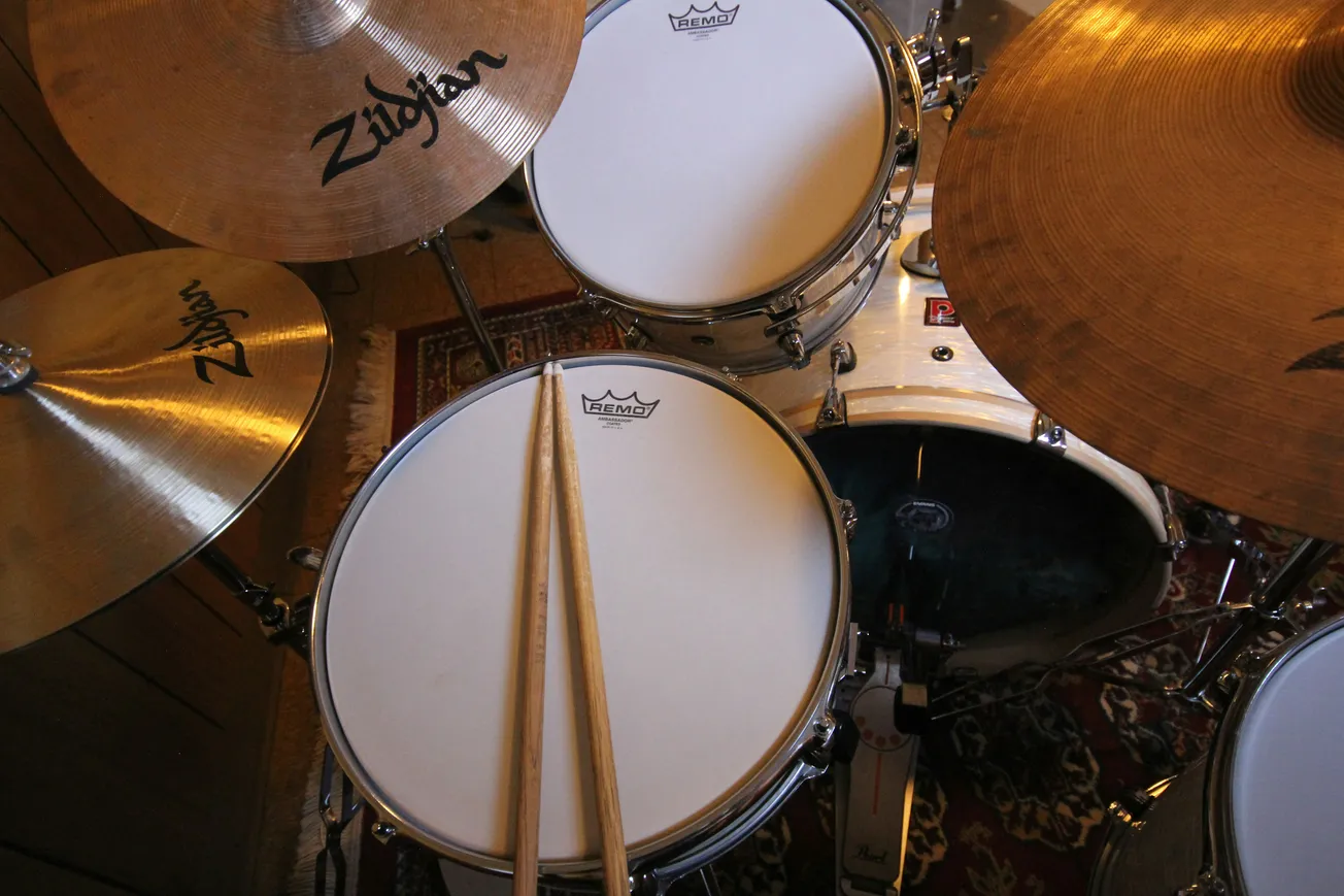 Close-up of a drum set with Zildjian cymbals and Remo drumheads. Two drumsticks rest on the snare. The setting suggests a relaxed, musical atmosphere.