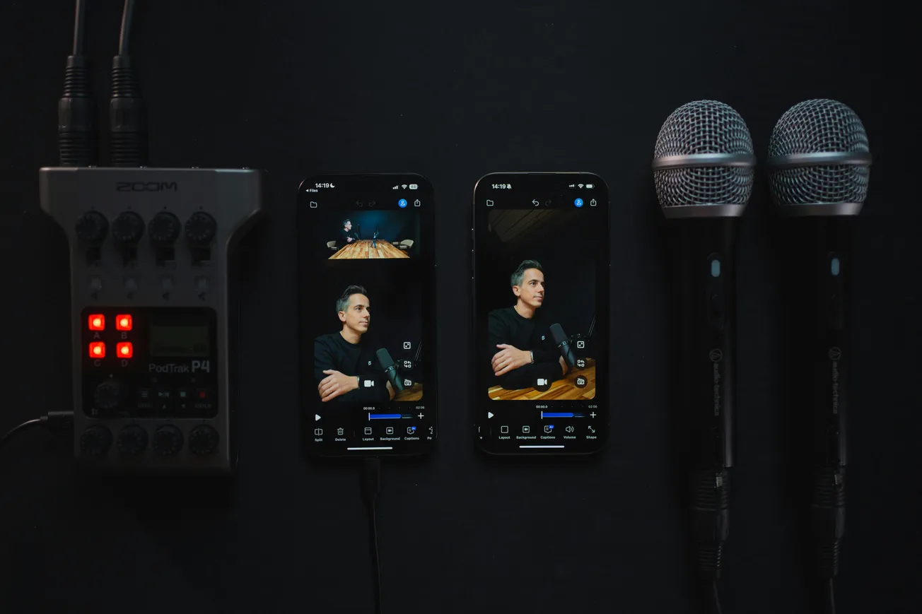 Audio equipment setup with two smartphones displaying a man speaking into a microphone. Nearby are two microphones and a Zoom PodTrak P4 recorder.