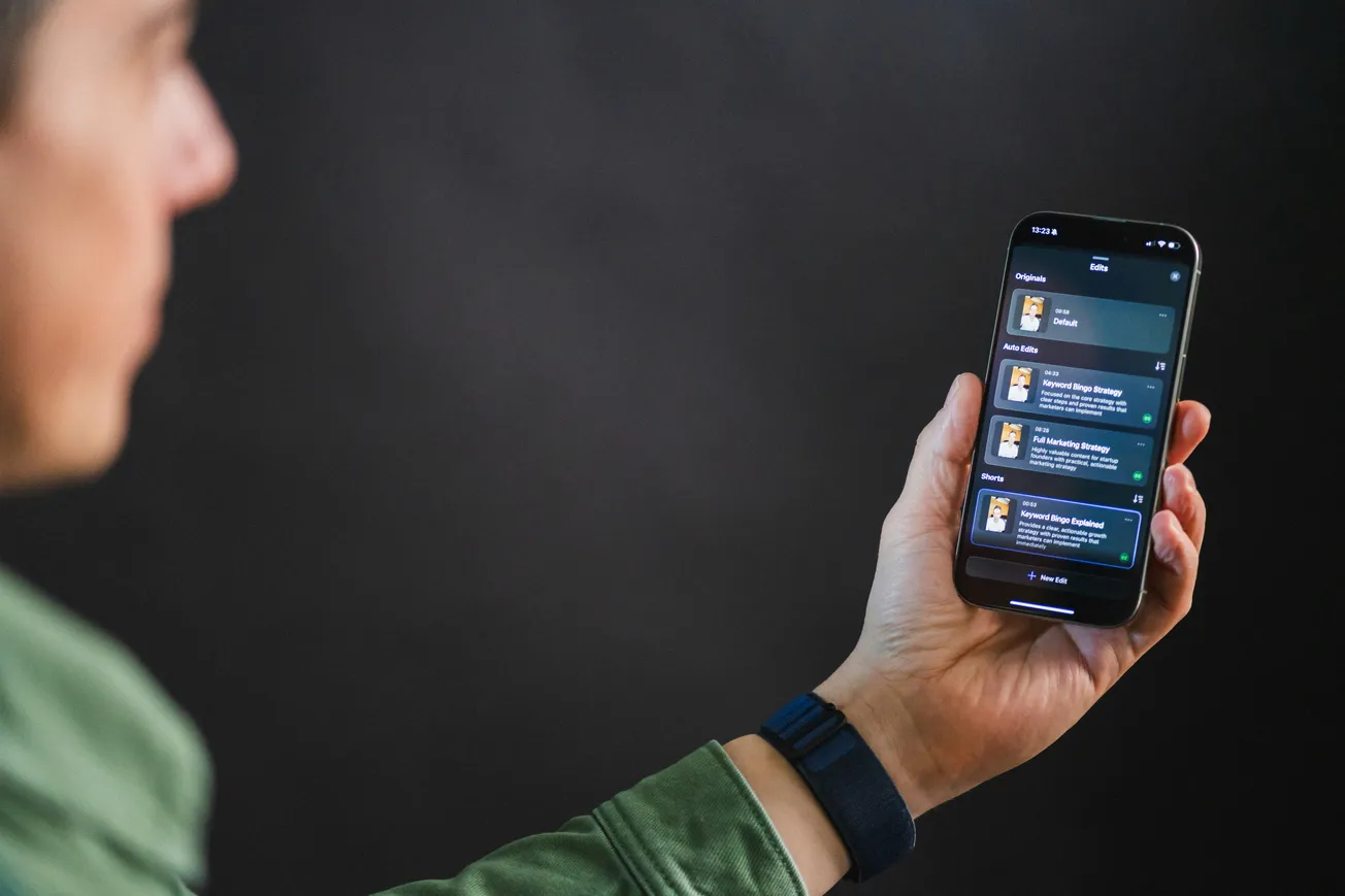 A person in a green jacket holds a smartphone showing a dark-themed app interface with text and icons. The background is softly blurred, creating a focused tone.