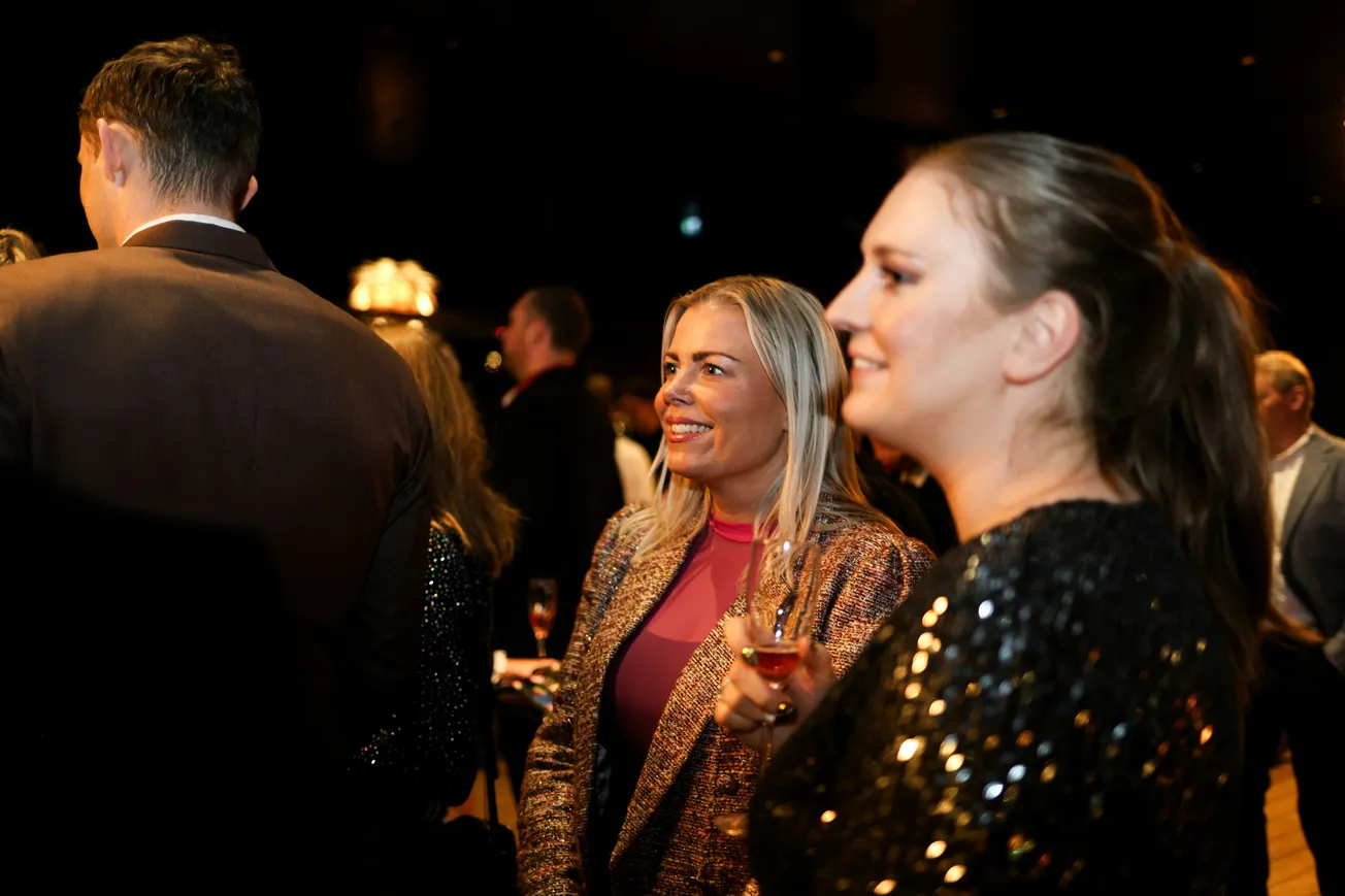 A festive gathering shows people smiling and mingling in elegant attire. A woman with a sparkling dress holds a drink, embodying joy and celebration.