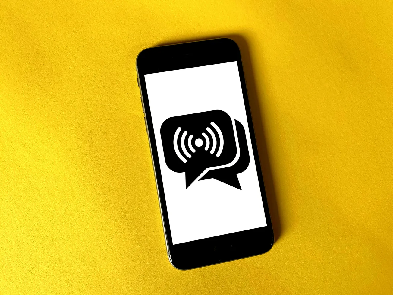 Smartphone on a yellow surface displaying a speech bubble with radio waves, symbolizing wireless communication and connectivity.