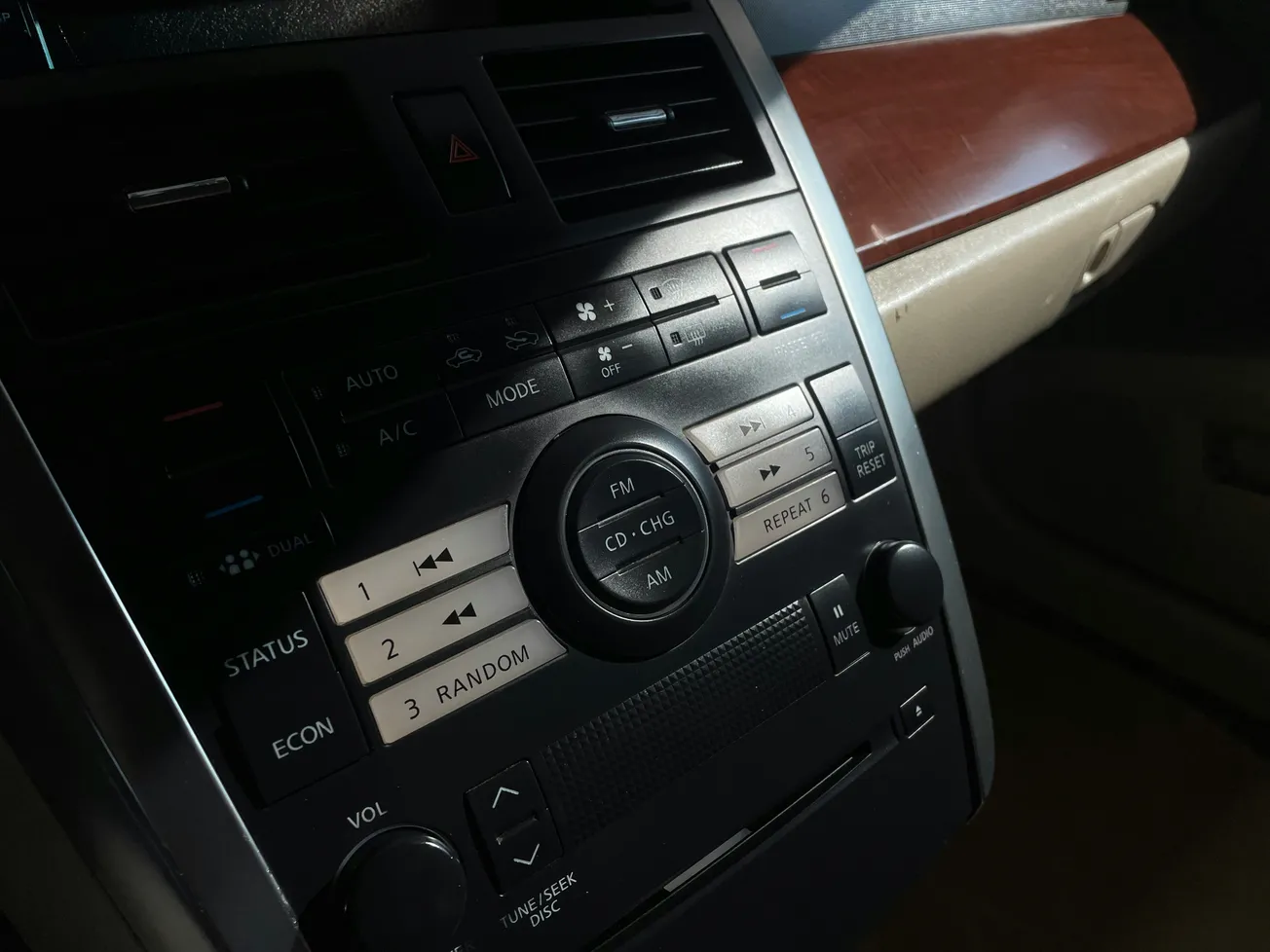 Close-up of a car stereo and climate control interface, featuring buttons for FM, CD, AC, and more. Warm lighting highlights the wood trim.
