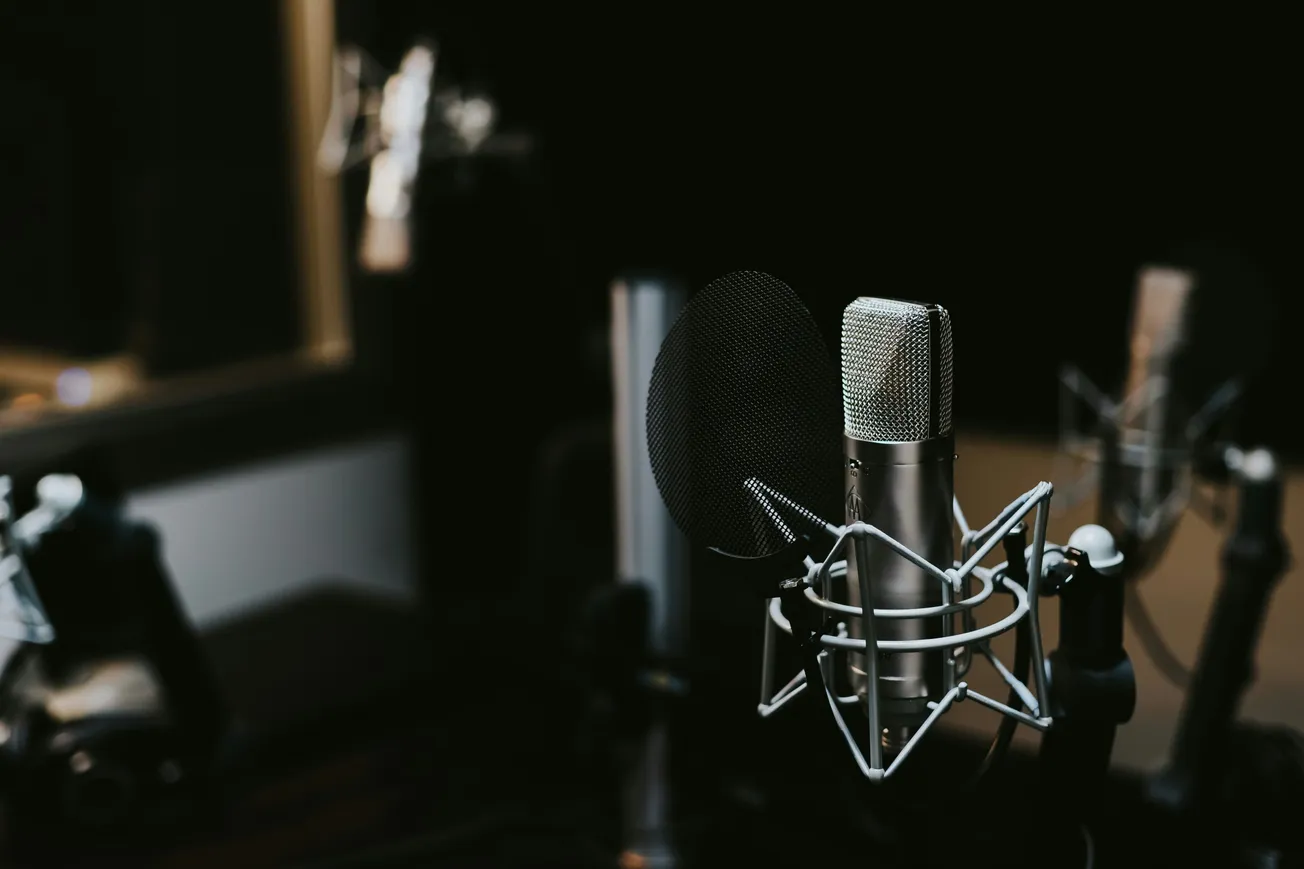 Close-up of a silver microphone with a pop filter in a dimly lit recording studio, conveying a professional and focused atmosphere.