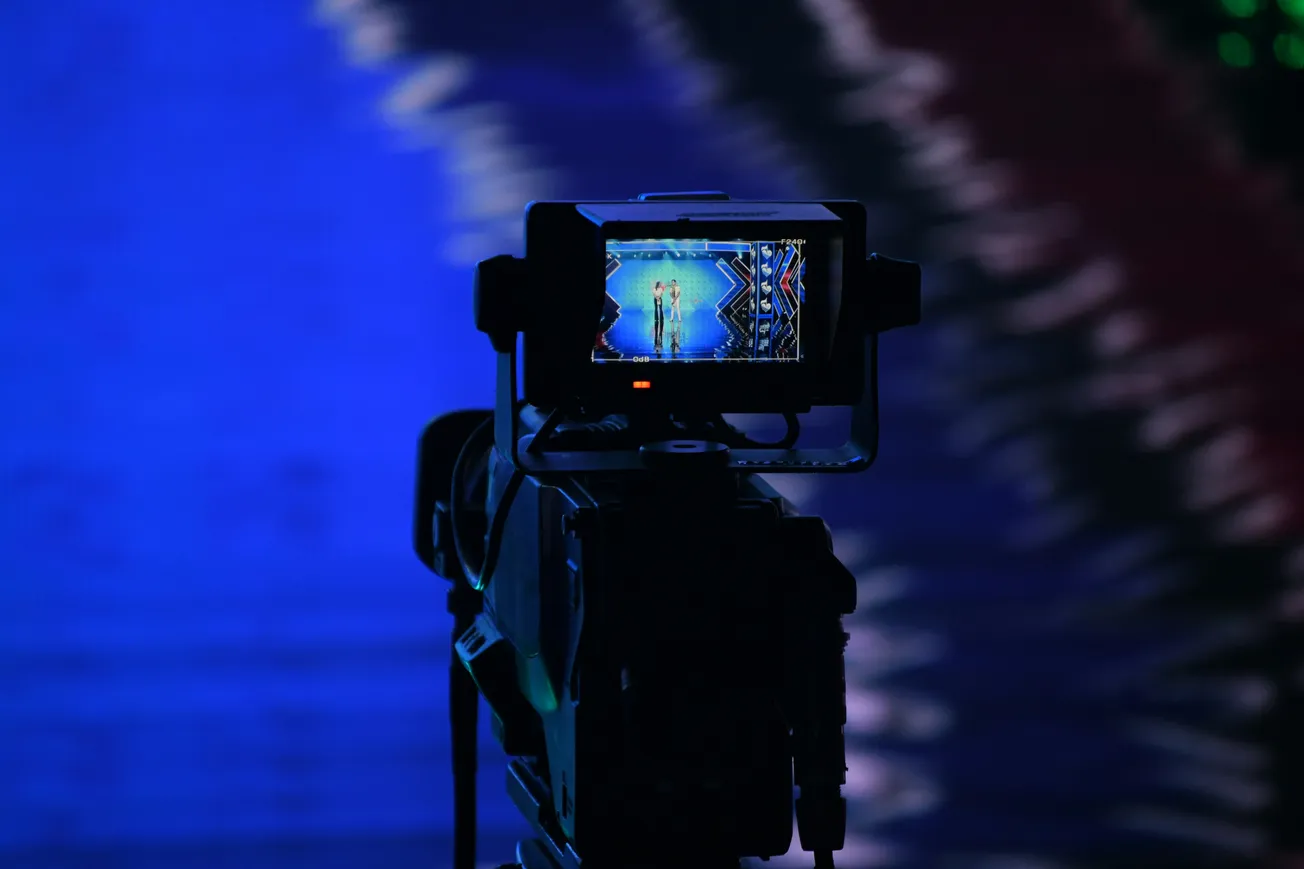 A camera focuses on a stage with vibrant blue lighting on its screen. The background is richly blurred, emphasizing a dynamic and professional ambiance.