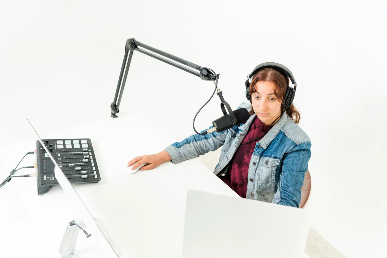 podcaster reviewing podcast industry news on laptop with microphone and headphones