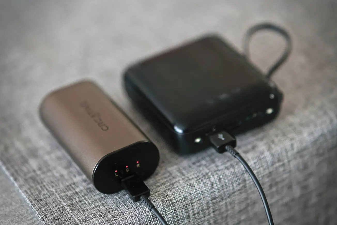 A brown portable charger and a black power bank sit on a gray fabric surface, both connected with charging cables, conveying a tech-savvy atmosphere.