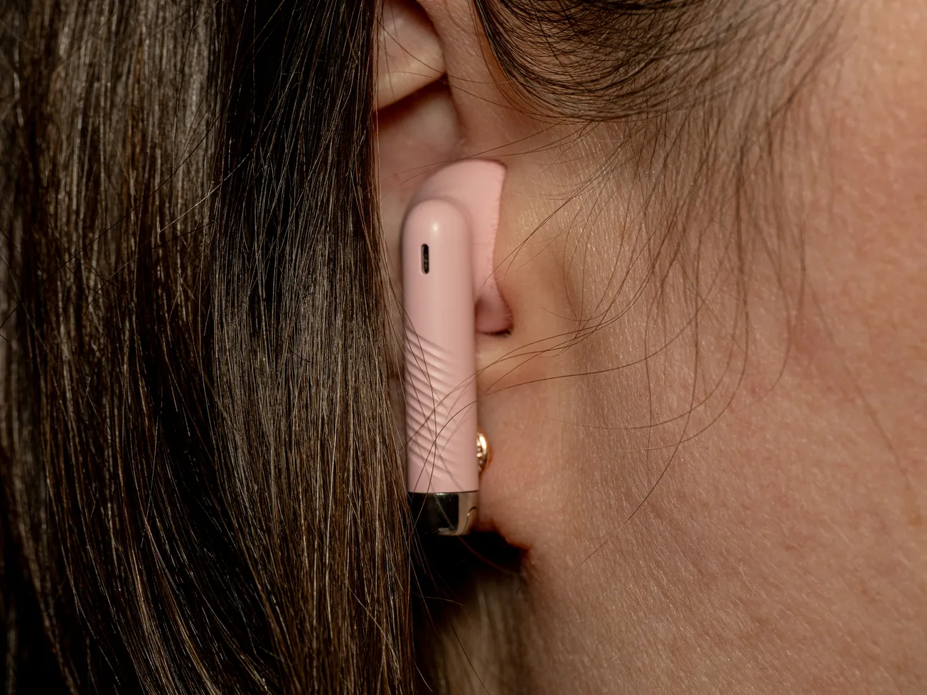 Close-up of a person wearing a pink wireless earbud in their ear. The focus is on the earbud, highlighting its sleek design against the hair and skin.